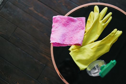 drain-cleaning From above of yellow latex gloves placed near rag and spray detergent on table against wooden floor in daytime